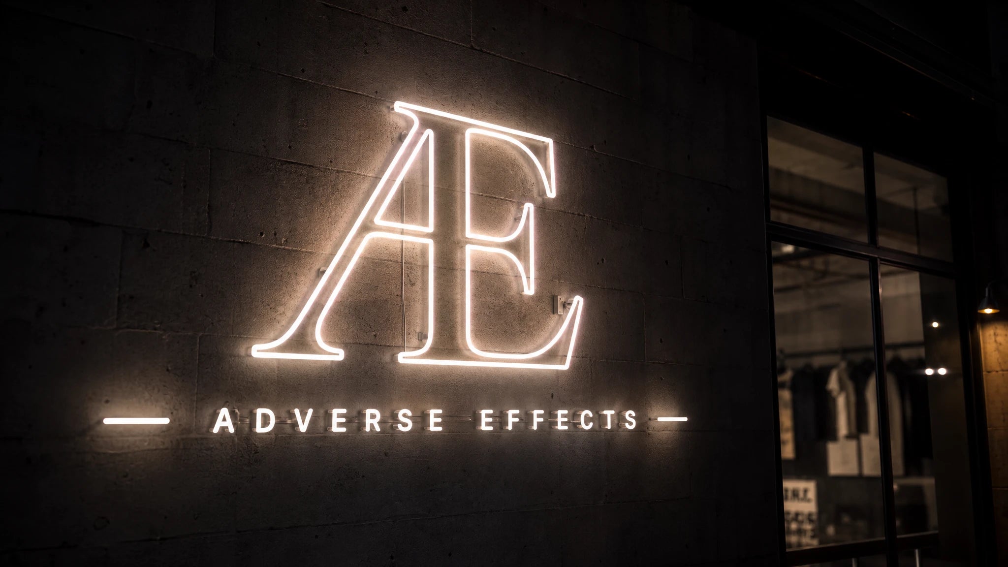 An illuminated AE monogram and Adverse Effects wordmark on a dark textured wall.