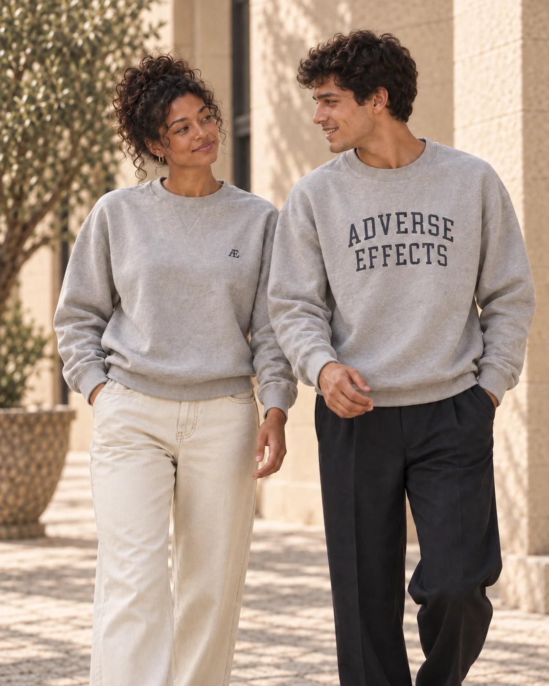 Two people in AE crewnecks sharing a relaxed conversation, wearing ecru denim and dark trousers.